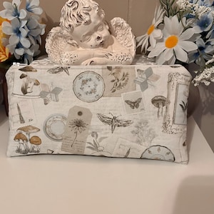 May include: A rectangular fabric zipper pouch featuring a collage print of vintage-style illustrations including mushrooms, butterflies, moths, floral plates, postage stamps, and handwritten script text on a light cream-colored background.