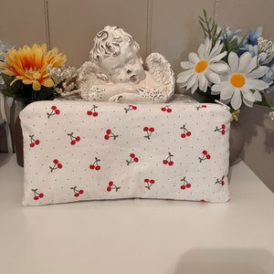 May include: White zippered pouch with a cherry print. The pouch is made of fabric and has a white background with red cherries.