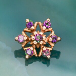 May include: A gold snowflake-shaped body jewelry piece with purple and green gemstones.