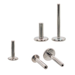 May include: Several silver-colored labret studs with flat disc backs and straight posts are displayed against a white background. The posts vary in length, and one stud has a visible hole at the end of the post. These body jewelry pieces are designed for lip or other facial piercings.