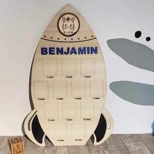 Op de afbeelding: Houten raketvormige groeicart met een zebra-illustratie en de naam "BENJAMIN" in blauwe letters. De kaart heeft 12 vakjes voor foto's, elk gelabeld met een maand in het Frans.