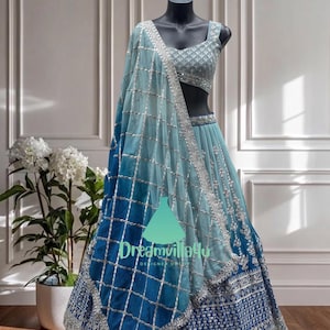 Puede incluir: Un conjunto lehenga choli azul claro y azul marino sobre un maniquí. El conjunto presenta intrincados bordados plateados y una dupatta a juego. La falda lehenga tiene un efecto degradado, que va del azul claro al azul marino.
