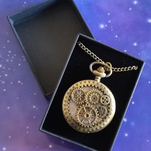May include: A bronze steampunk pocket watch with visible gears, presented in a black box. The watch has a chain and is set against a starry purple background. The watch face features intricate gear designs.