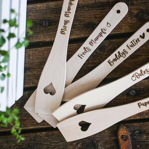Könnte beinhalten: Vier Holzlöffel mit Herz-Ausschnitten und personalisierten Namen: "Mitras Mampfi", "Freds Mampfi", "Baddys Futter" und "Odes Food".