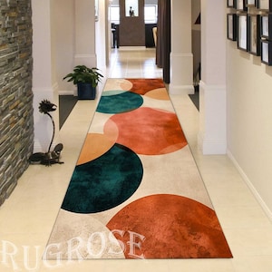 Può includere: Un tappeto da corridoio lungo e rettangolare con un motivo geometrico di cerchi sovrapposti in tonalità di arancione, rosso, verde acqua e beige. Il tappeto è disposto in un corridoio con pareti bianche e pavimento in pietra.