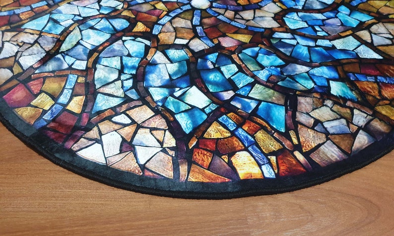 May include: A round rug with a stained glass design featuring blue, brown, and gold colours. The rug has a black border.