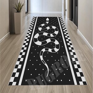 May include: Black runner rug featuring a white snake design with a dotted background. The rug has a checkered border and white stripes. The rug is placed in a hallway with wooden flooring.