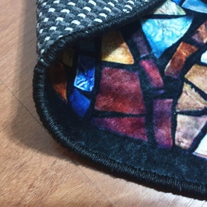 May include: Close-up of a round rug with a stained glass design. The rug has a black border and a black and white chequered backing.