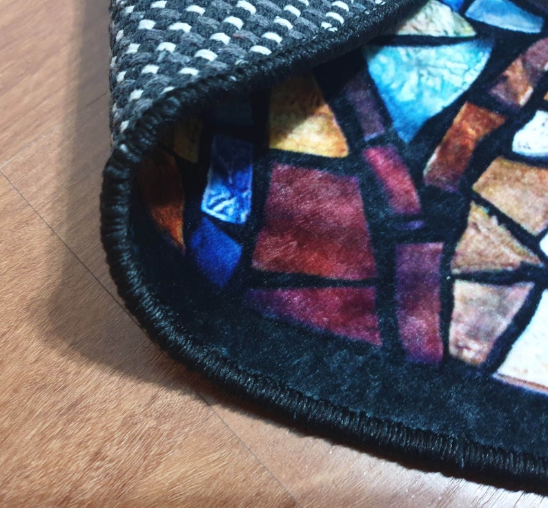May include: Close-up of a round rug with a stained glass design. The rug has a black border and a black and white chequered backing.