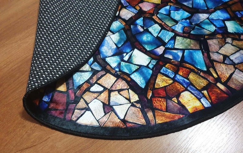 May include: A round rug with a stained glass design featuring a variety of colours, including blue, red, yellow, and brown. The rug has a black border and a non-slip backing.