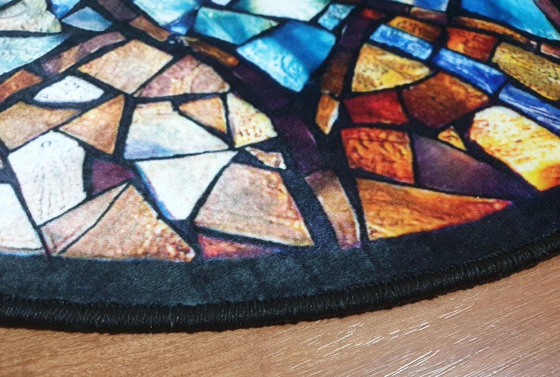 May include: A round rug with a stained glass design featuring a variety of colours, including blue, red, orange, and yellow. The rug has a black border with a stitched edge.