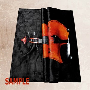 K&ouml;nnte beinhalten: Ein schwarzer Samtstoff mit einem gedruckten Bild einer Geige. Die Geige ist orange und braun mit schwarzen Saiten. Der Stoff ist in der Mitte gefaltet und das Wort "SAMPLE" ist in der linken unteren Ecke gedruckt.