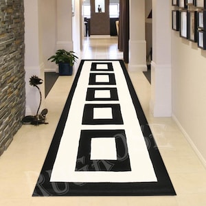 May include: Black and white runner rug with a geometric pattern of squares. The rug has a white background with black squares and a black border.