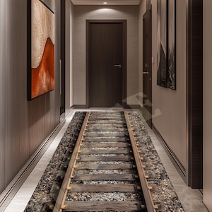 May include: A hallway runner rug with a realistic railroad track design. The rug features wooden railroad ties and gravel, creating a three-dimensional effect. The rug is placed in a hallway with wooden paneling and artwork.