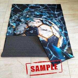 May include: A black and blue rug with a cracked glass design and a soccer ball in the center. The rug has a black backing with a grid pattern. The word "SAMPLE" is stamped in red on the rug.