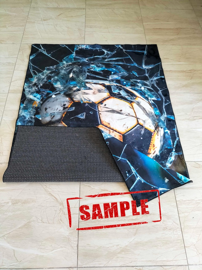May include: A black and blue rug with a cracked glass design and a soccer ball in the center. The rug has a black backing with a grid pattern. The word "SAMPLE" is stamped in red on the rug.