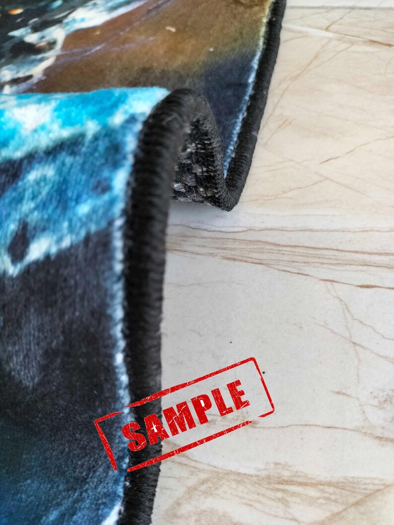 May include: Close-up of the edge of a blue and black rug with a black border. The rug has a galaxy-like pattern. The word "SAMPLE" is stamped in red on the rug.