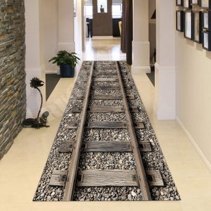Peut inclure: Tapis rectangulaire avec un motif imprimé en 3D de voie ferrée. Le tapis présente des détails réalistes de traverses en bois, de gravier et de rails métalliques. La palette de couleurs comprend des nuances de gris, de marron et de beige, créant un aspect texturé et réaliste. Idéal pour un couloir ou une entrée.