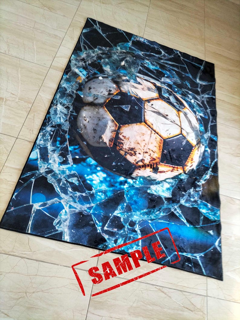 May include: A black and blue rug with a cracked glass design and a soccer ball in the center. The soccer ball is brown and white with black stitching. The rug has the word "SAMPLE" stamped in red on the bottom right corner.