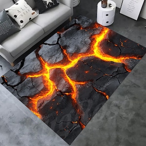 May include: A rectangular rug with a design resembling molten lava. The rug has a dark grey, cracked surface with vibrant orange and yellow streaks, creating a fiery, textured effect. The rug is placed on a grey floor.