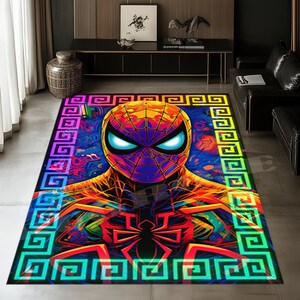 Puede incluir: Una alfombra rectangular que presenta un gráfico vibrante y multicolor de una máscara de superhéroe con ojos blancos brillantes. El diseño incluye un emblema de araña central y un borde con patrón de greca en colores neón azul, naranja y amarillo.
