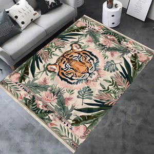 May include: A beige rug with a tiger face in the center surrounded by green and pink tropical leaves. The tiger has orange and black stripes.