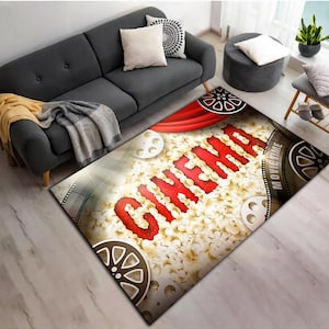 May include: A red and white rug featuring the word "CINEMA" in large red letters. The rug is decorated with popcorn, film reels, and a red curtain.