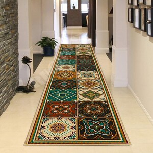 Può includere: Un lungo tappeto rettangolare per corridoio con un motivo ripetuto di colorati disegni geometrici a piastrelle. Il tappeto presenta un bordo beige e una varietà di colori tra cui verde acqua, arancione, marrone e crema. Il tappeto è posto in un corridoio con pareti bianche e pavimento chiaro.