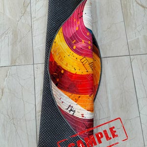 May include: A rolled up round rug with a colorful abstract design featuring musical notes and a black border. The rug is labeled "SAMPLE".