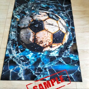 May include: A black and blue rug with a large, weathered soccer ball breaking through a cracked glass pane. The word "SAMPLE" is stamped in red across the bottom of the rug.