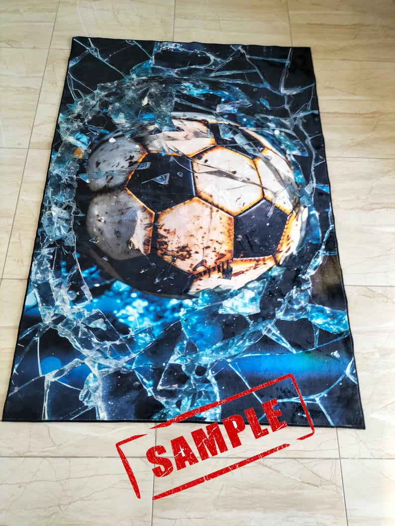 May include: A black and blue rug with a large, weathered soccer ball breaking through a cracked glass pane. The word "SAMPLE" is stamped in red across the bottom of the rug.