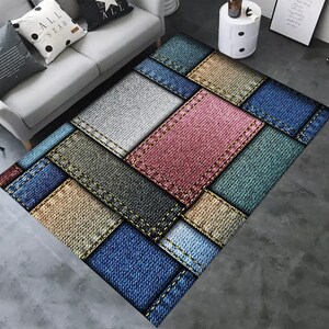 May include: A patchwork rug with a denim design. The rug is made up of squares of different colors of denim, including blue, grey, beige, and pink. The squares are sewn together with yellow stitching.