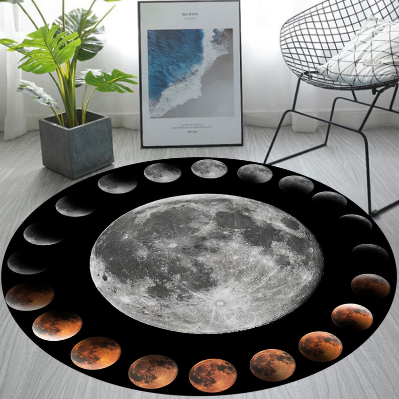 May include: A round black and white rug featuring a large full moon in the centre surrounded by a ring of crescent moons in various phases. The rug has a black background with a white moon and a ring of orange crescent moons.