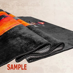K&ouml;nnte beinhalten: Ein schwarzer Teppich mit einem farbenfrohen Design, das eine Gitarre und Flammen zeigt. Der Teppich hat einen schwarzen Rand und ist in drei Teile gefaltet. Das Wort "SAMPLE" ist in Rot auf wei&szlig;em Hintergrund unter dem Teppich gedruckt.