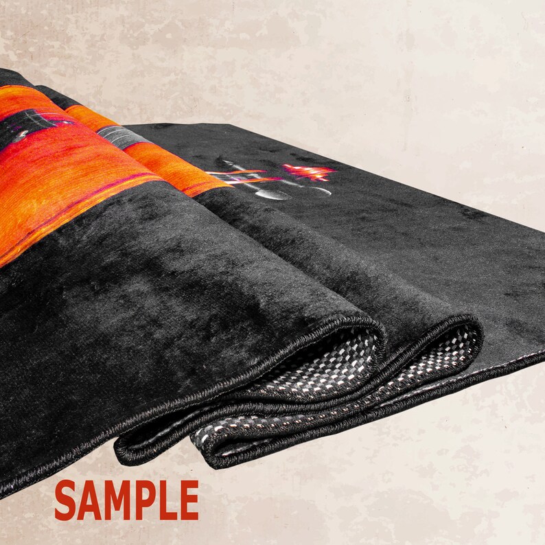 K&ouml;nnte beinhalten: Ein schwarzer Teppich mit einem farbenfrohen Design, das eine Gitarre und Flammen zeigt. Der Teppich hat einen schwarzen Rand und ist in drei Teile gefaltet. Das Wort "SAMPLE" ist in Rot auf wei&szlig;em Hintergrund unter dem Teppich gedruckt.
