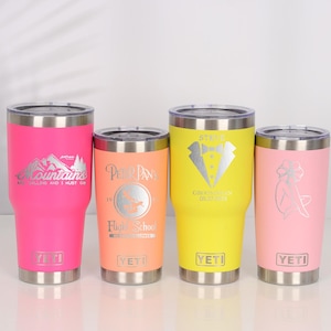 Op de afbeelding: Vier geïsoleerde bekers in levendige kleuren: felroze, oranje, geel en lichtroze. Elke beker heeft een zilveren ontwerp en tekst, waaronder een berglandschap, Peter Pan, een smoking en een vrouw. De bekers hebben een zilveren rand en de merknaam.