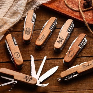 May include: Several personalised wooden pocket knives with names engraved on the wooden handles. The knives are open, showing their tools, and are arranged on a wooden surface.