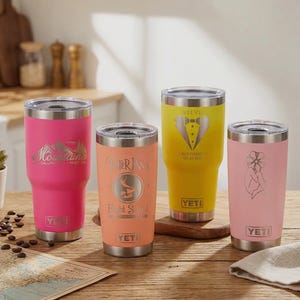 May include: Four stainless steel insulated tumblers in pink, peach, yellow, and pink. Each tumbler has a silver lid and a unique design, including mountain graphics, a deer, a bow tie, and a floral illustration. The tumblers are on a wooden surface.
