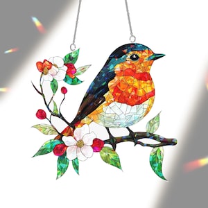 May include: Stained glass bird suncatcher with a colorful design. The bird features shades of orange, red, blue, and white, perched on a branch with white flowers and green leaves. Includes a silver chain for hanging.
