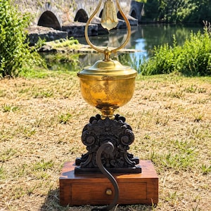May include: A vintage coffee grinder featuring a rectangular wooden base with a small drawer, a black cast iron mechanism with ornate scrollwork, and a polished brass hopper with a matching brass lid and a decorative arched handle on top.