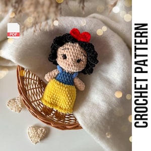 May include: Crochet pattern for a Snow White amigurumi doll. The doll is wearing a yellow skirt, blue bodice, and a red bow. The pattern is available as a PDF download.