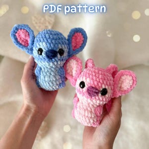 May include: Two plush crochet figures, one blue and one pink, featuring large ears with pink inner accents, dark button eyes, and small noses. The text PDF pattern is visible at the top. These soft, textured toys are crafted with yarn.