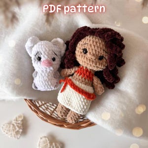 May include: A crochet doll with dark brown curly hair and a tan complexion, wearing an orange top and white skirt, alongside a small white crochet pig with a pink nose. The text "PDF pattern" is visible at the top of the image.