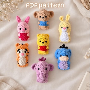 Può includere: Una collezione di sette piccole marionette da dito all'uncinetto che raffigurano vari personaggi animali in filato rosa, beige, giallo, arancione, blu e viola. Il testo PDF pattern è visibile in alto. Ogni marionetta ha occhi a perla neri.