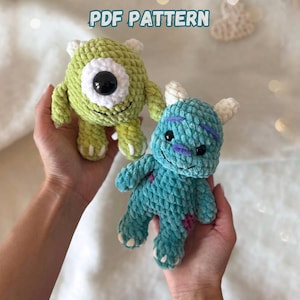 Puede incluir: Dos juguetes de ganchillo de felpa que presentan un monstruo redondo de color verde lima con un gran ojo central y un monstruo azul cerceta con manchas moradas y dos cuernos. El texto PDF PATTERN aparece arriba en letras azules.