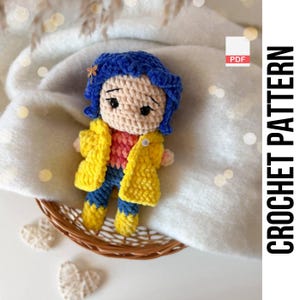 May include: A crocheted doll with blue hair, a yellow jacket, and blue trousers. The doll is in a woven basket. The image includes the text "CROCHET PATTERN" printed vertically on the right side.