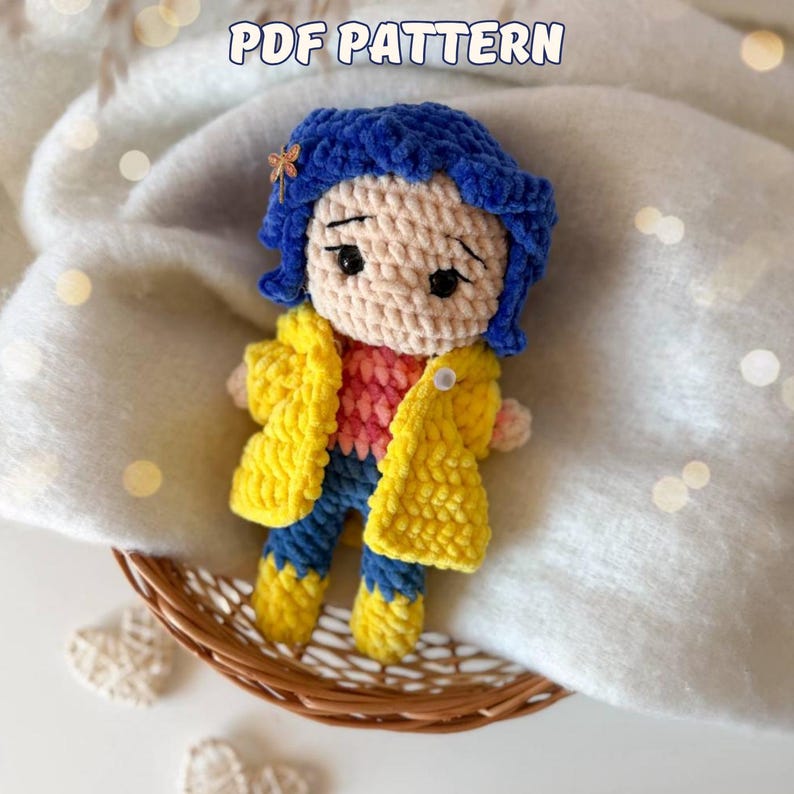 May include: A crochet doll with blue hair, a small dragonfly hair clip, a yellow coat, a pink patterned shirt, and blue pants. The doll has black embroidered eyes and eyebrows. The text PDF PATTERN is visible at the top of the image.