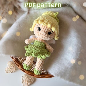 May include: A crochet doll with pale skin, yellow hair styled in a bun, and a green dress. The doll has black embroidered eyes and small white wings on its back. The text "PDF pattern" is visible at the top of the image.