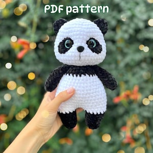 May include: A crochet panda plush toy featuring a white body and head with black ears, black eye patches, black arms, and black legs. The panda has large, dark, glossy eyes and a small black nose. The text PDF pattern is visible at the top.