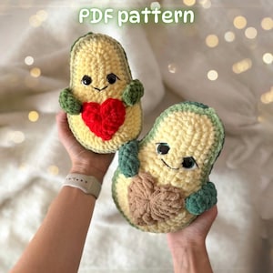 Pode incluir: Dois peluches de abacate feitos em crochê com casca verde-escura e centro amarelo-claro. Um abacate segura um coração vermelho vivo, enquanto o outro segura um coração bege. Ambos têm olhos e sorrisos bordados. O texto diz PDF pattern.